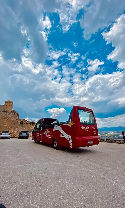 Red open-top tour bus parked outside of Palamidi Castle in Nafplio