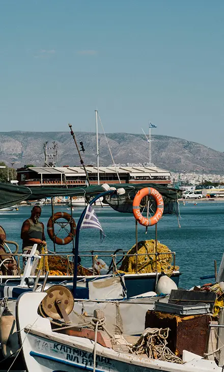 Traditional Greek fishing boat in a harbour and a fisherman in the background fixing his nets