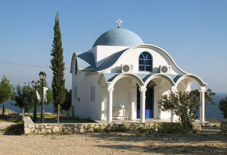The white and blue church of Agia Kiriaki in Tolo, surrounded by trees