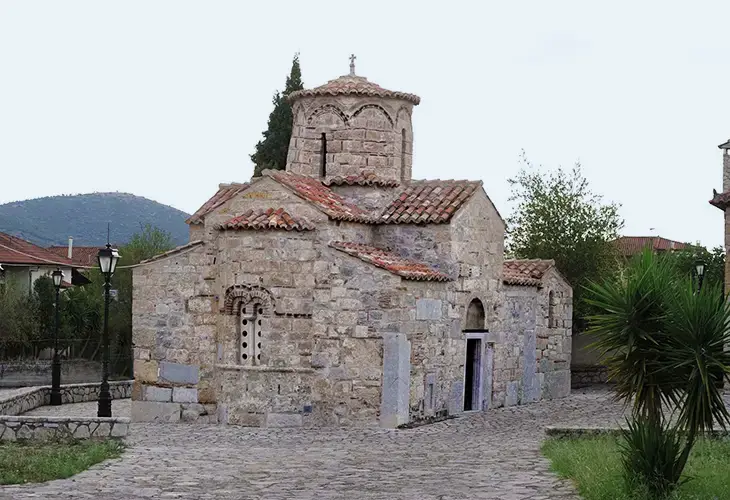 A old, stone chapel in Agia Moni monastery in Aria surrounded by plants and other buildings