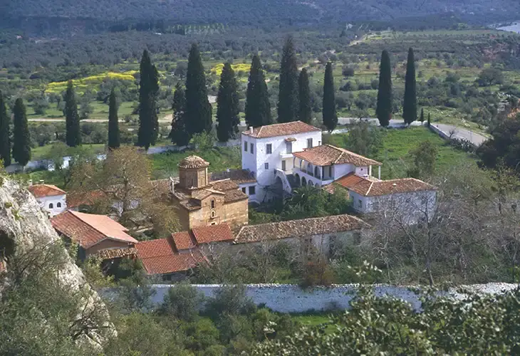 A stone church surrounded by trees and then by the monastery's white buildings
