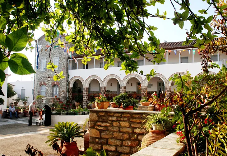 Photo of Monastery Agion Anargyron in Ermioni with arches full of plants and a nun with man having a conversation in the background