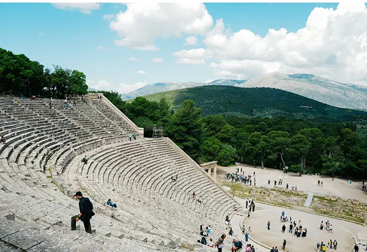 View of Epidaurus ancient theatre from the top middle part, people standing in the middle and a person walking up on the left