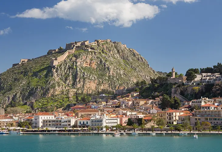 View of Nafplio, seaside town from the water with Palamidi Castle on a hill on the right and the clock tower above the old town
