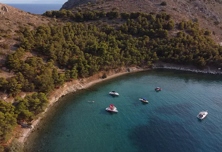 Romvi Island beach in Tolo, surrounded by a small pine forest and little boats