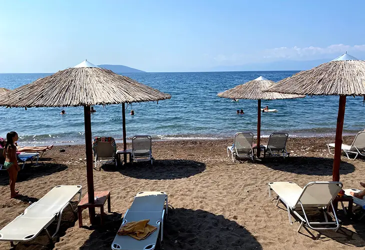 Dark sanded beach in Kandia, with sunbeds, umbrellas and an unobstructed view of the blue water