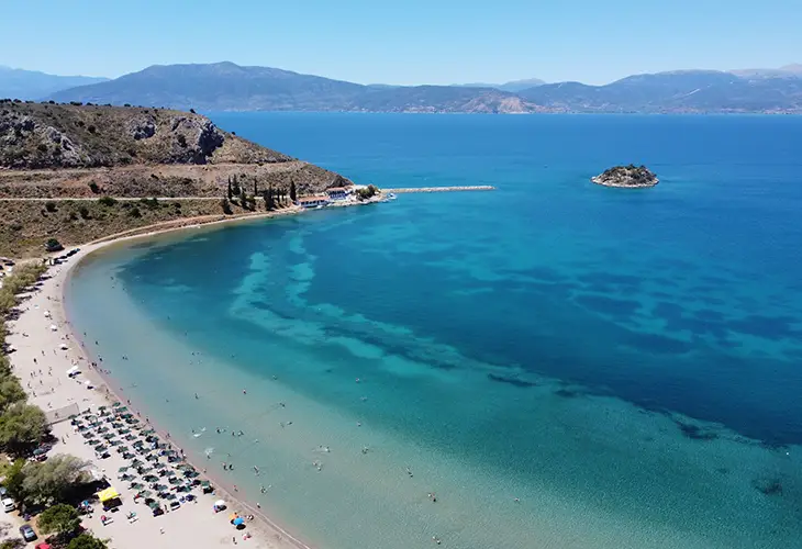 A long and wide beach in a halfmoon shape and a small island in the background