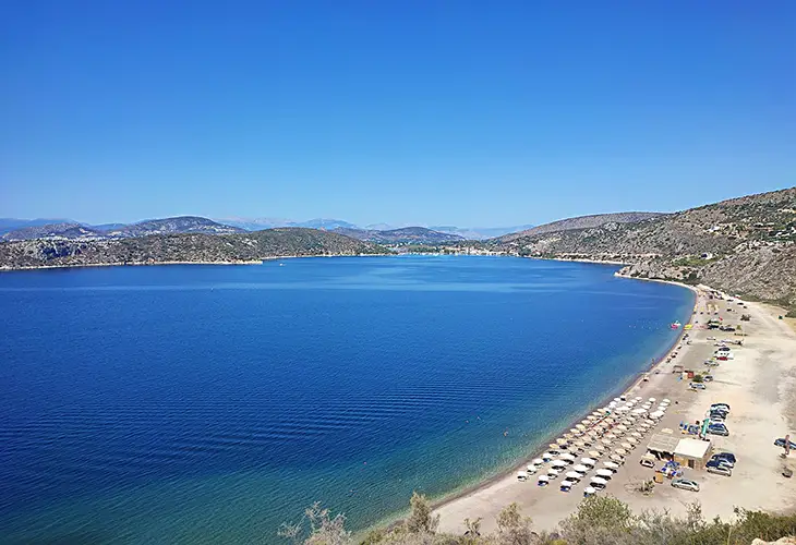 A long, white sand beach in a protected cove, two beach bars and a few cars parked behind