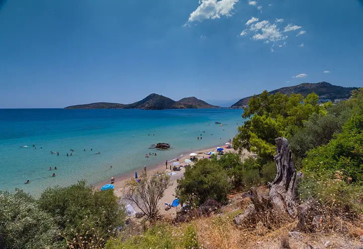 View of Tolo beach, trees, turquoise waters and the islets of Tolo in the background