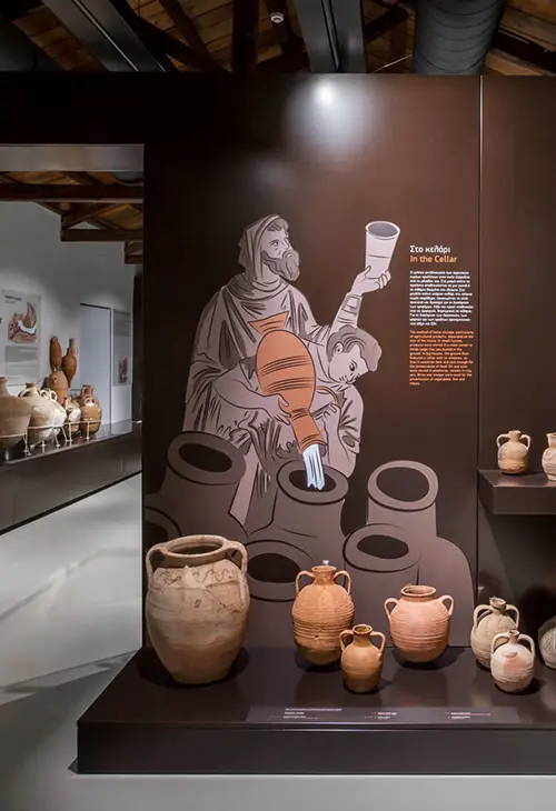 Interior of the Byzantine Museum in Argos with various pottery exhibits, and a drawing of a man on the wall using said pottery