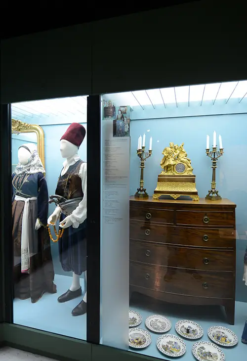 Two mannequin dressed with traditional outfits on the right, old furniture and house decorations on the left, found at the Folklore Museum in Nafplio